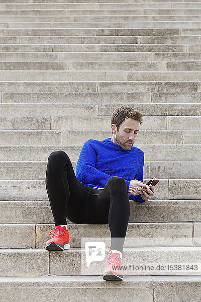 Jogger  der auf Stufen sitzt und ein Smartphone benutzt