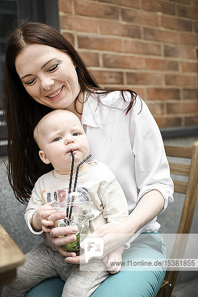 Smiling mother with her baby boy drinking lemonade