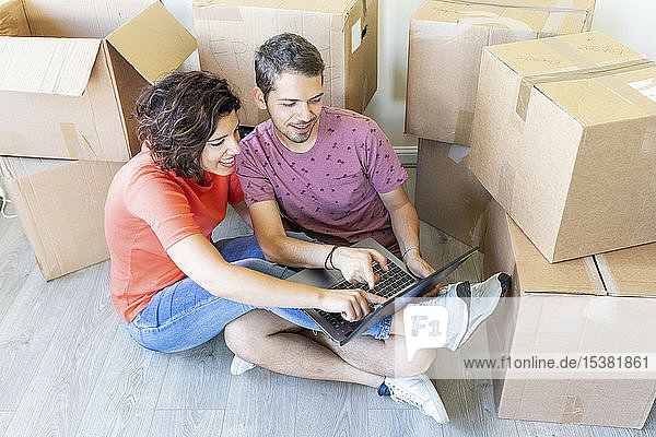 Happy couple moving into new home using laptop