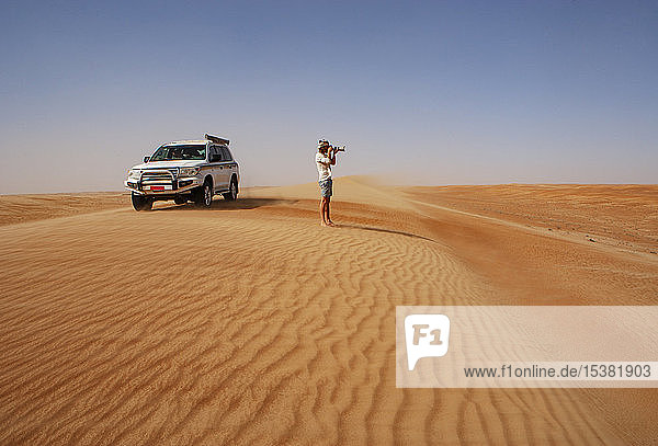 Mann beim Fotografieren in der Wüste  neben einem Geländewagen  Wahiba Sands  Oman