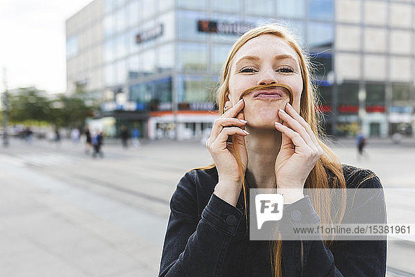 Portrait of redheaded young woman making mustache with her hair  Berlin  Germany