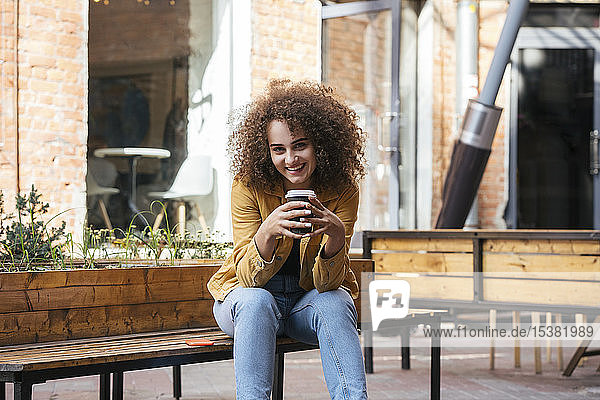 Portrait of smiling teenage girl sitting on bench with coffee to go