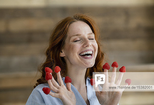Porträt einer lachenden rothaarigen Frau mit Himbeeren an den Fingerspitzen