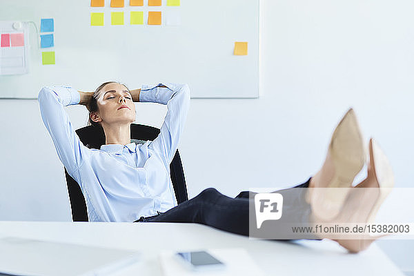Junge Geschäftsfrau entspannt im Büro mit den Füßen auf dem Schreibtisch liegend
