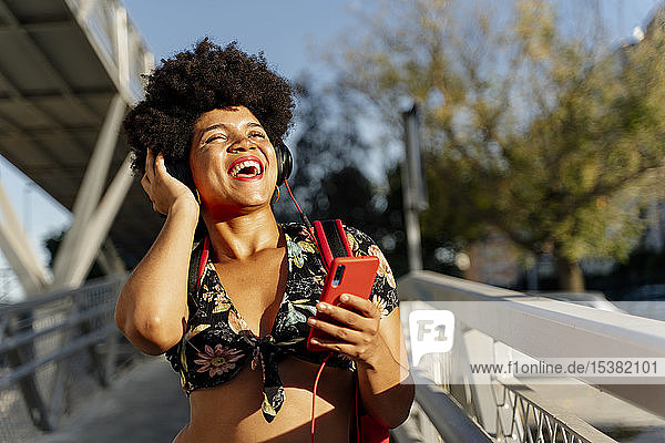 Lachende afro-amerikanische Frau mit Kopfhörern und Smartphone beim Musikhören