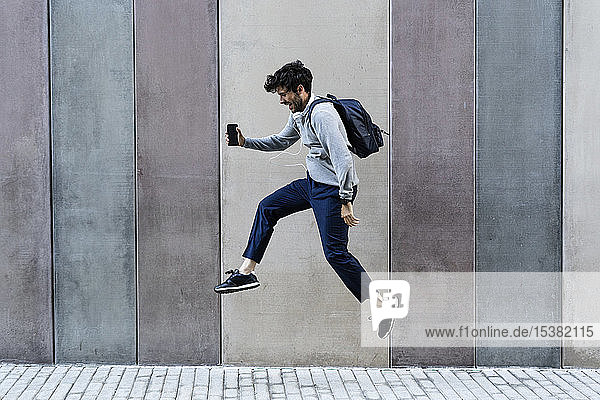 Glücklicher Mann hält Handy und springt vor eine Wand