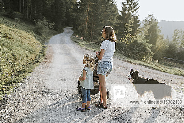 Mutter mit Tochter  Kinderwagen und Hund auf Waldweg stehend