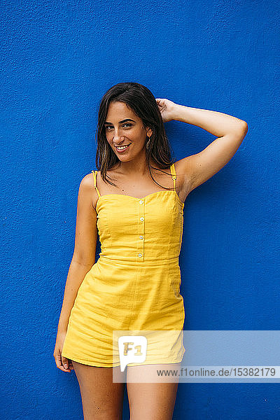 Porträt einer schönen jungen Frau in gelbem Kleid  die an einer blauen Wand posiert