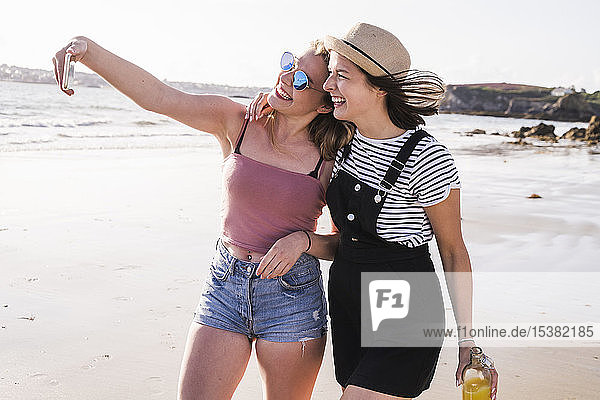 Two girlfriends having fun  walking on the beach  taking smartphone selfies