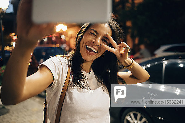 Junge Frau  die nachts in der Stadt ein Smartphone benutzt und ein Selfie