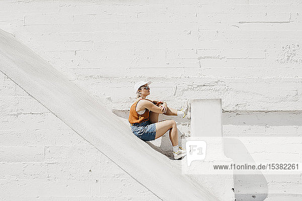 Junge Frau sitzt vor einer weißen Wand im Freien