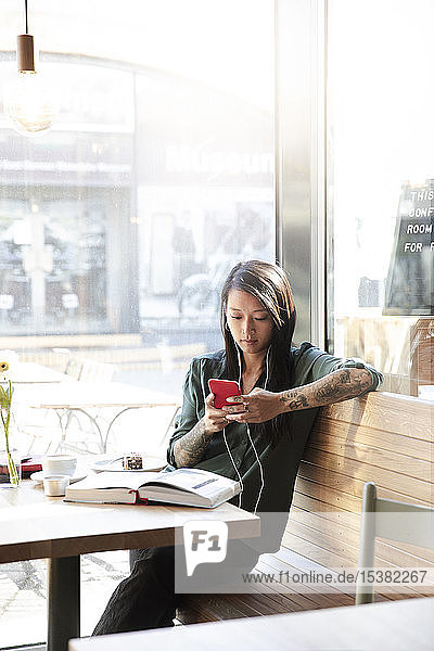 Frau mit Ohrstöpseln und Handy in einem Cafe