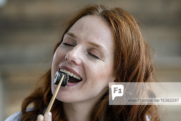 Porträt einer glücklichen rothaarigen Frau beim Sushi-Essen