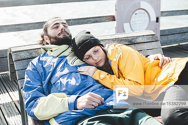Couple lying with closed eyes on a wooden bench at the beach