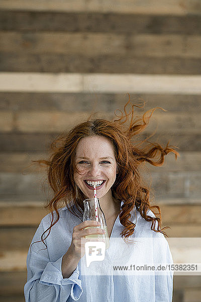 Porträt einer lachenden rothaarigen Frau mit wehenden Haaren  die Limonade trinkt