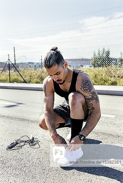 Sporty young man tying shoes before training on a road