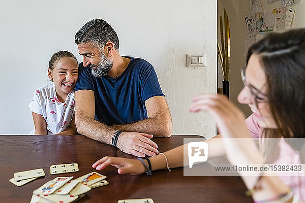 Glücklicher Vater mit zwei Töchtern  die zu Hause auf einem Holztisch Karten spielen