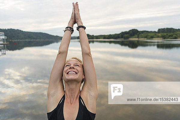 Glückliche junge Frau hebt ihre Arme an einem See