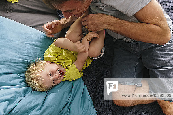 Father cuddling and tickling son on bed