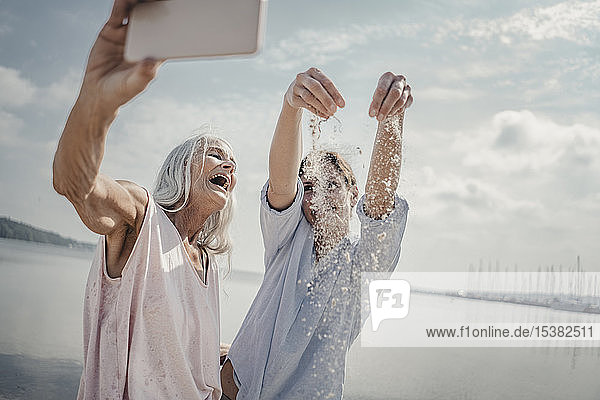 Mutter und Tochter amüsieren sich am Strand  indem sie sich selbst ein Smartphone nehmen