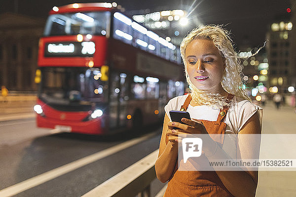 Junge Frau in London schaut nachts auf ihr Smartphone