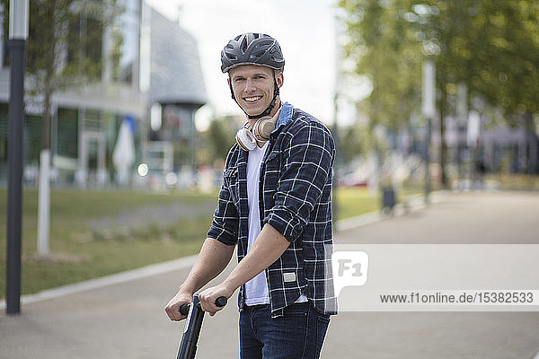 Porträt eines lächelnden jungen Mannes mit E-Scooter in der Stadt