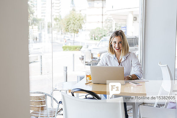 Porträt einer lächelnden jungen Frau mit Laptop auf einem Tisch in einem Cafe