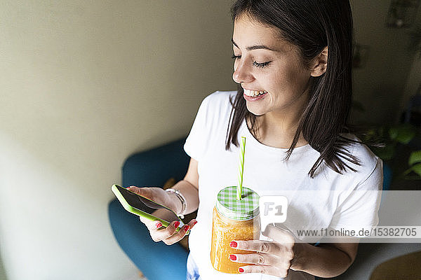 Glückliche junge Frau mit einem Smoothie  die in einem Café mit ihrem Handy telefoniert