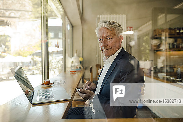 Portrait of senior businessman with cell phone and laptop in a cafe