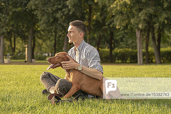 junger Mann mit seinem Hund  kuschelnd auf einer Wiese