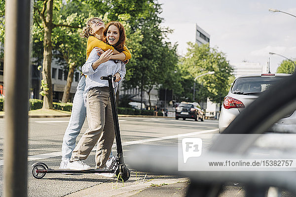 Junge Frau umarmt Freundin auf E-Scooter in der Stadt