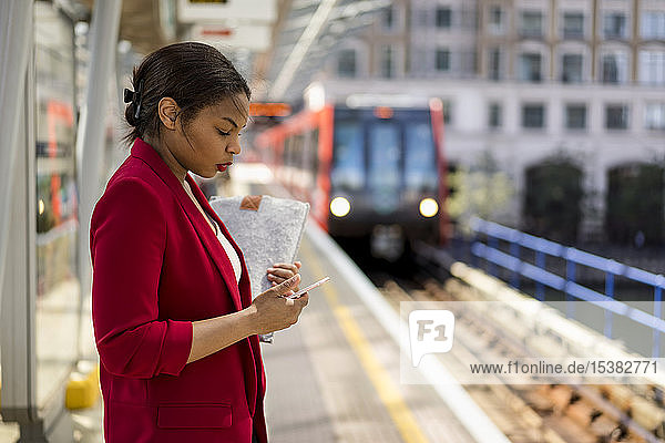 Businesswoman standing on platform looking at mobile phone  London  UK