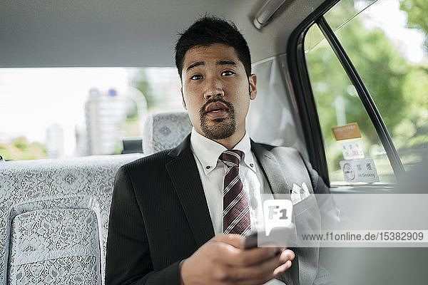 Junger Geschäftsmann mit Handy im Taxi im Gespräch mit dem Fahrer