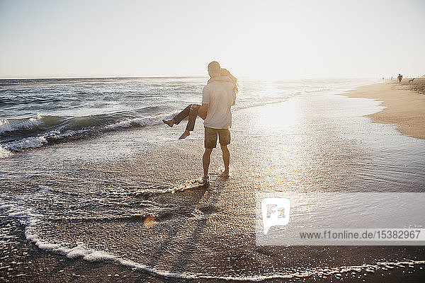 Glücklicher junger Mann mit Freundin bei Sonnenuntergang am Meeresufer