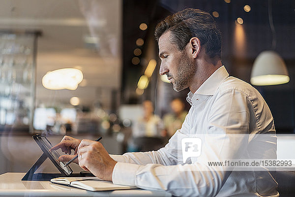 Businessman using tablet and taking notes in a cafe