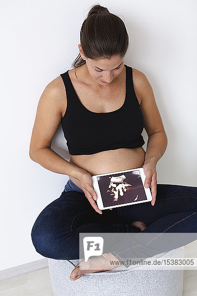 Junge schwangere Frau mit Ultraschallbild ihres ungeborenen Babys auf der Tablette
