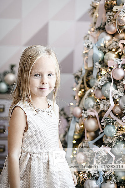 Portrait of smiling little girl standing in front of lighted Christmas tree