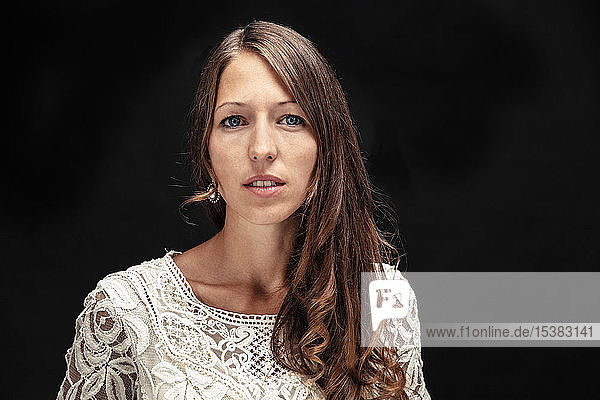 Portrait of young woman with long brown hair against black background