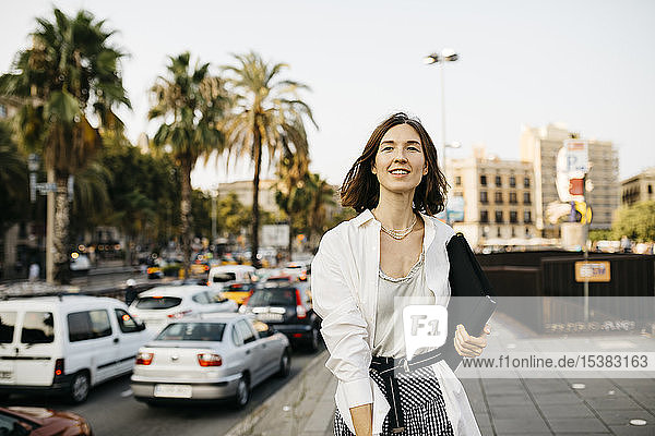 Hübsche Geschäftsfrau mit Mappe  die in der Stadt spazieren geht