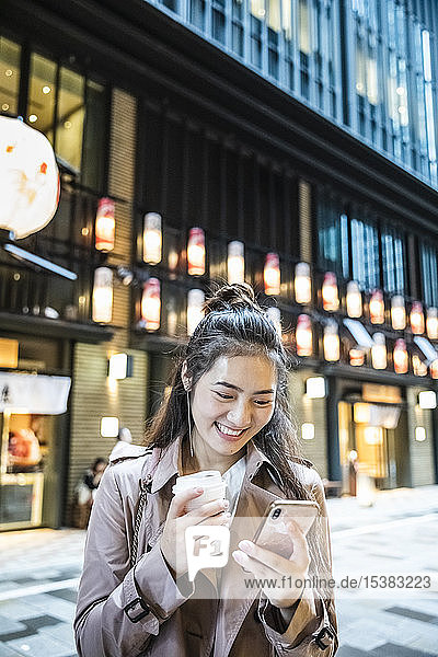 Glückliche junge Frau mit einem Getränk zum Mitnehmen und einem Smartphone in Ginza  Tokio  Japan