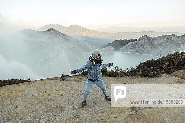 Young boy with respirator masks standing at the edge of volcano Ijen with arms outstretched  Java  Indonesia