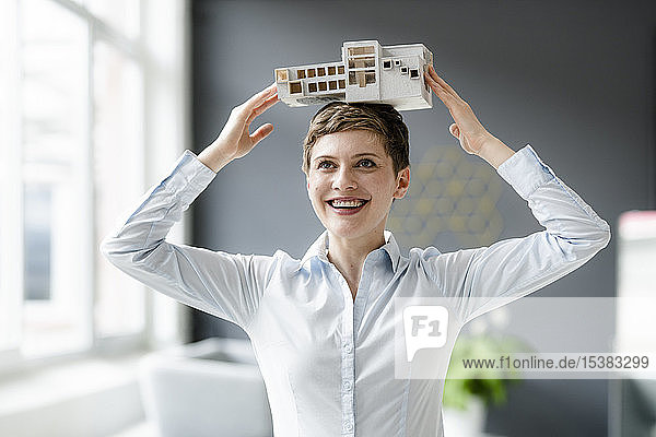 Glückliche Geschäftsfrau trägt Architekturmodell auf dem Kopf