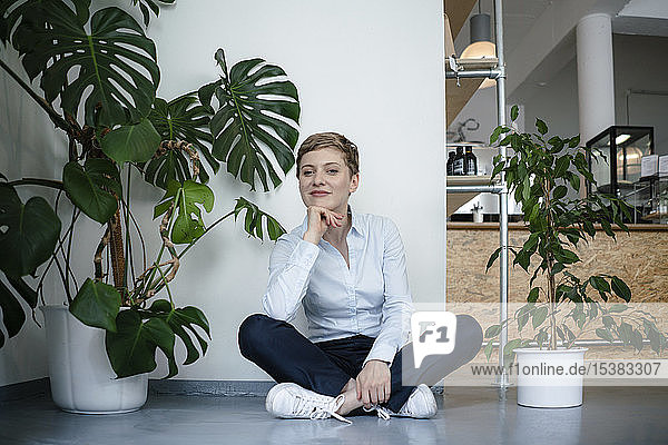 Porträt einer Geschäftsfrau  die auf dem Boden sitzend von Pflanzen umgeben ist