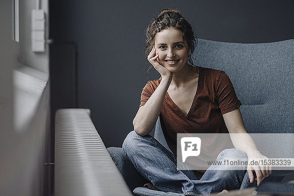 Porträt einer lächelnden jungen Frau  die zu Hause auf einem Liegestuhl sitzt