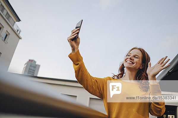 Lächelnde rothaarige Frau benutzt Mobiltelefon auf der Dachterrasse