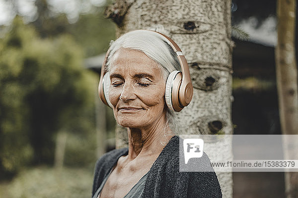 Ältere Frau entspannt sich in der Natur  hört Musik mit Kopfhörern