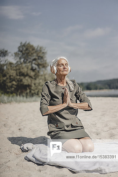 Senior woman meditating with headphones on the beach