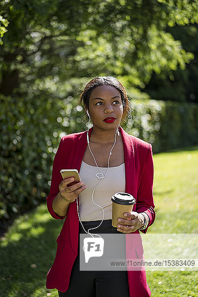 Porträt einer Geschäftsfrau mit Kaffee zum Mitnehmen  die mit Smartphone und Kopfhörern Musik hört  London  UK