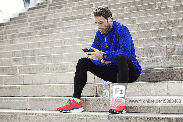 Jogger sitting on steps and using smartphone
