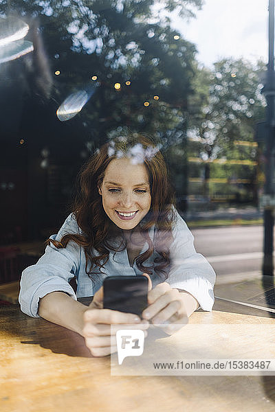 Glückliche rothaarige Frau mit Handy in einem Cafe
